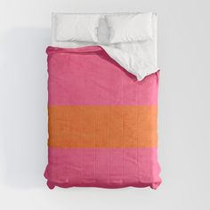 a pink and orange bed spread with two pillows on top of it, against a white wall