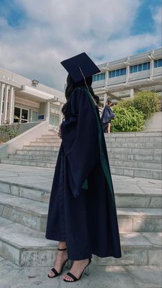 a woman in a graduation gown standing on some steps and looking up at the sky