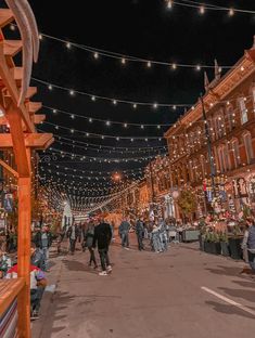 people are walking down the street in front of buildings with lights strung over them at night