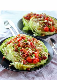 two black plates filled with lettuce and tomatoes on top of a white table cloth