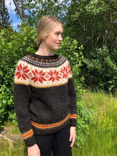 a woman standing in the grass wearing a sweater with red and yellow flowers on it