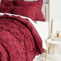 a bed with red comforter and pillows in a white room next to a table