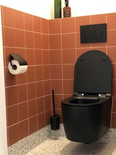 a black toilet sitting in a bathroom next to a wall mounted toilet paper dispenser