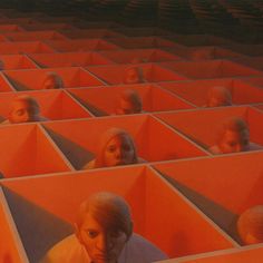 two people are sitting in the middle of an orange room with rows of identical heads