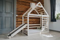 a white bunk bed with a slide next to it in front of a wooden wall