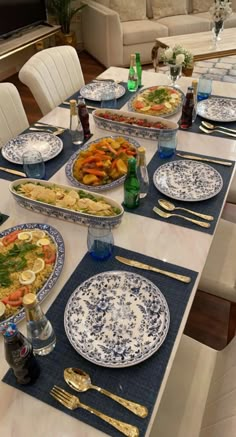 a table set with blue and white plates, silverware and gold cutlery on it