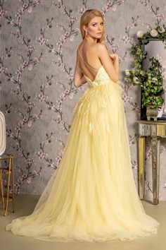 a woman in a yellow dress standing next to a wall with flowers on it's back