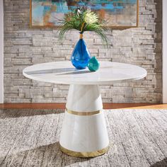 a white table with a blue vase on it in front of a brick wall and rug