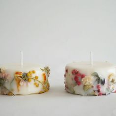 two candles with flowers on them sitting next to each other in front of a white background