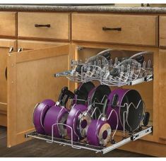 an open dish rack with purple pots and pans in the bottom drawer on a wooden kitchen countertop