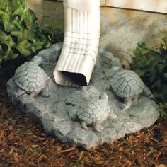 three little turtle statues sitting on top of a stone slab next to plants and bushes