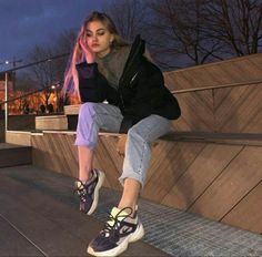 a woman with pink hair is sitting on a bench and looking at the camera while wearing sneakers