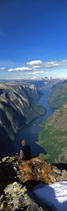 a person sitting on top of a mountain looking down at the valley and lake below