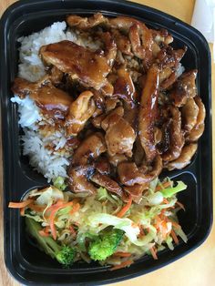 a black plate topped with rice and meat next to broccoli covered in sauce