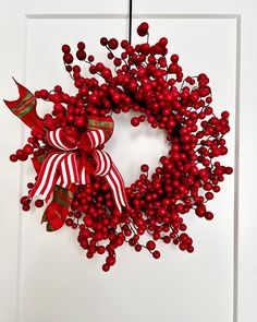 a wreath with red berries and bows hanging on a door