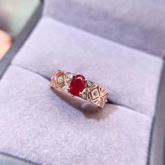 a gold ring with a red stone sits in a velvet box on top of a table