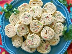 a blue plate topped with rolls covered in cheese and vegetables on top of a colorful table cloth