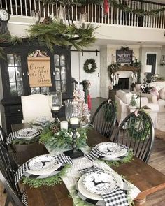 the dining room table is set for christmas with black and white plates, greenery and candles