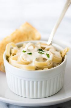 a white bowl filled with pasta and sauce on top of a plate next to bread