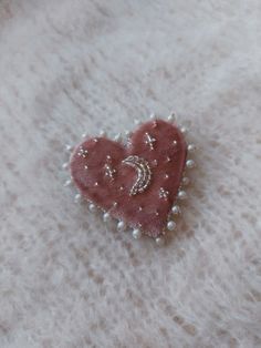 a heart shaped brooch sitting on top of a white fur covered surface with pearls