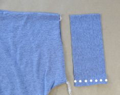 two pieces of blue fabric with white buttons on them, one piece has been cut off and the other part is being sewn