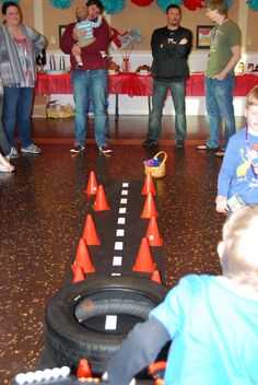 a group of people standing around in a room with toy cars and orange cones on the floor