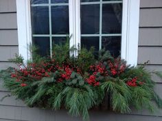 a window box filled with red berries and greenery in front of a gray house