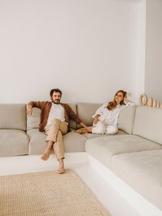 a man and woman sitting on top of a couch in front of a white wall