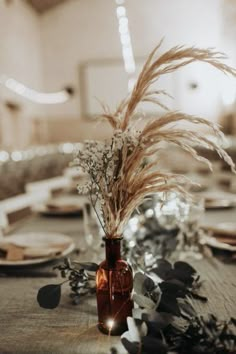 a vase filled with dried flowers on top of a wooden table covered in plates and napkins