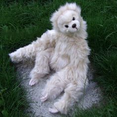 a white teddy bear sitting in the grass with its legs spread out and eyes wide open