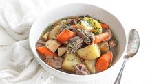 a white bowl filled with stew and carrots on top of a table next to a spoon