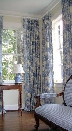 a bedroom with blue and white curtains on the windowsills, a bench in front of a window