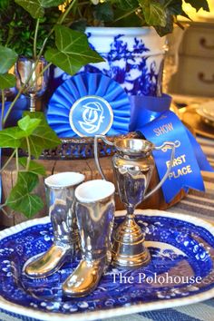 a blue and white plate topped with two silver cups next to a potted plant