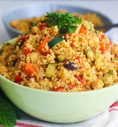 a bowl filled with rice and vegetables on top of a white table cloth next to two spoons