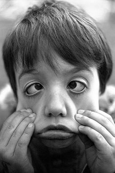 a young boy holding his hands to his face while looking at the camera with an intense look on his face