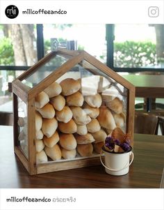 there is a small glass house with bread in it next to a coffee cup on the table