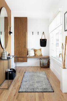 a room with wood floors, white walls and a mirror on the wall next to a bench