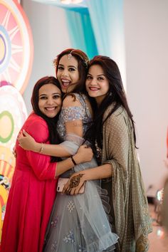 three young women hugging each other in front of a colorful wall with circles on it