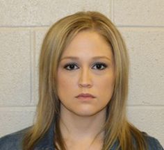 a woman with long blonde hair and blue shirt in front of a white brick wall