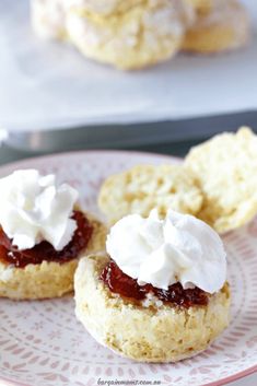 two biscuits with whipped cream and jelly on top sit on a pink plate next to cookies