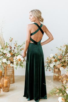 a woman standing in front of flowers wearing a dark green dress with cross back detail