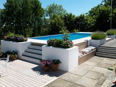 a woman sitting on the ground next to a swimming pool with plants growing in it