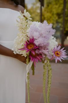 a bride holding a bouquet of flowers in her hand and wearing a white dress with purple accents