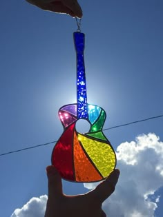 a hand holding a multicolored stained glass suncather in front of a blue sky