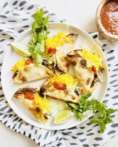 a white plate topped with quesadillas next to a bowl of sauce and cilantro