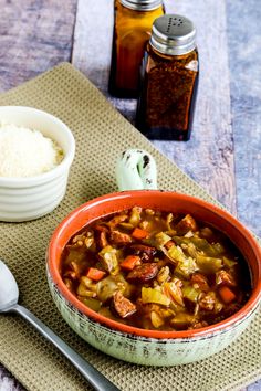 there is a bowl of stew next to a spoon and salt shaker on the table