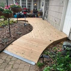 a wooden walkway in front of a house with lots of plants and flowers on the ground