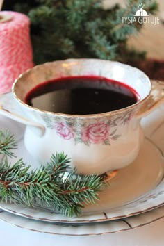 a cup of coffee on a saucer next to a plate with pine needles and berries