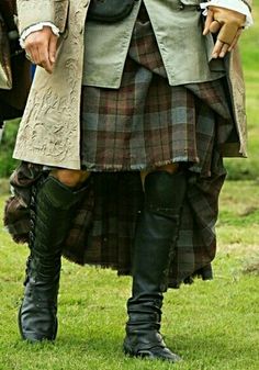 a man in a kilt and boots standing on the grass with other people behind him