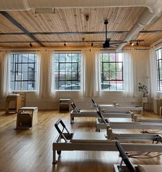 an empty room with several rows of beds in front of large windows and wooden floors